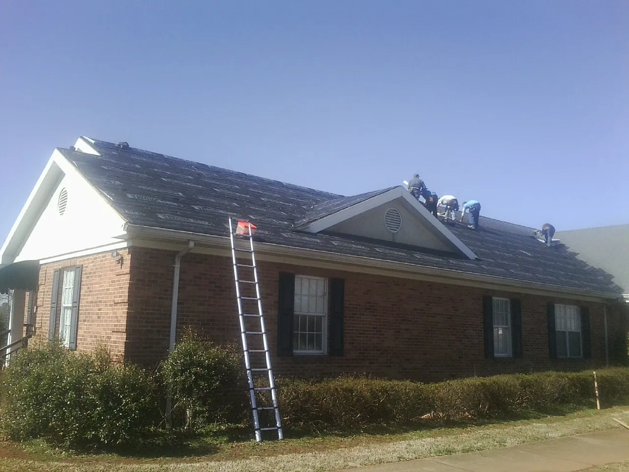 Crew tearing shingles off a brick ranch roof with a ladder set — Emergency Roof Repair work by our crew in Providence