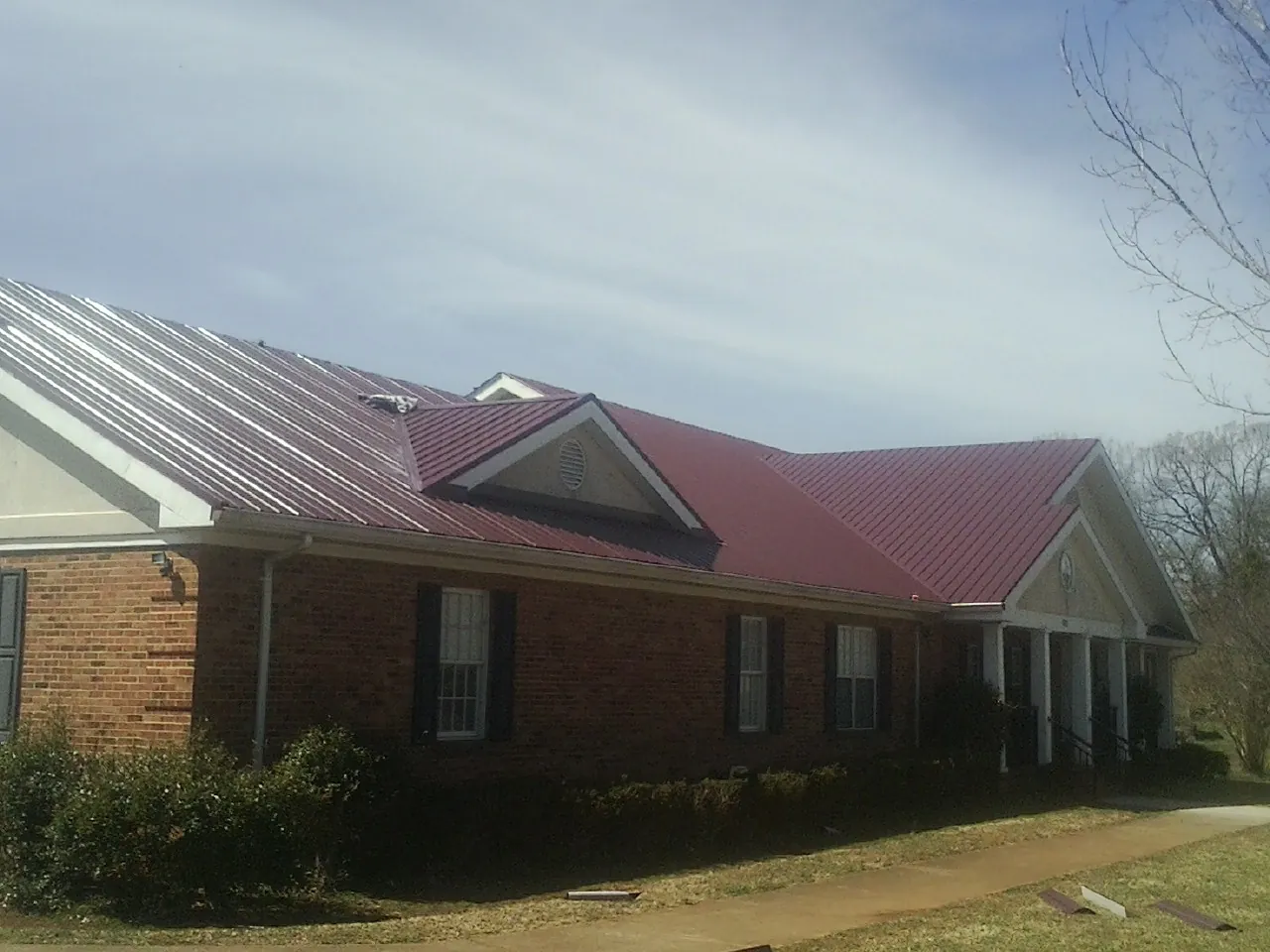 Red metal roof with gabled entries on a long brick building, from a Hail Damage Roof Repair job in Providence
