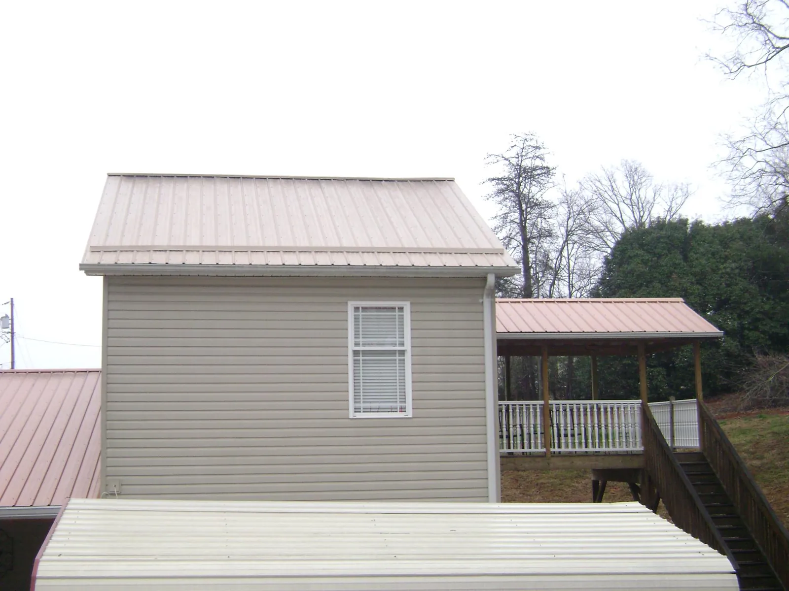 Tan metal roofs on a two story addition and attached porch, from a Roof Replacement job in Providence